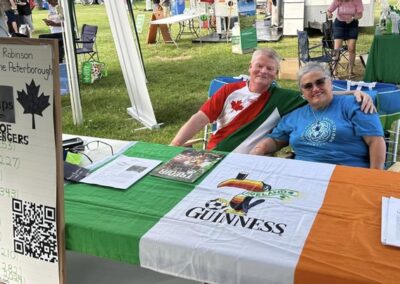 Jay and Rose sitting behind the booth of of Nine Ships Inc. during the Niagara Irish Festival. The table is adorned with the Irish flag and information about the bicentennial.