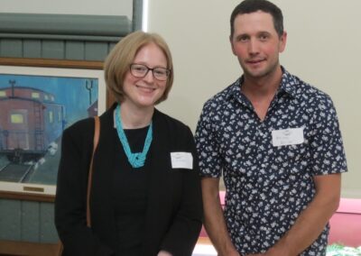 Consul General Janice McGann stands next to Patrick Leahy with smiles. In the background on the left a painting of a train car, a covered window and a small fern in the right corner.