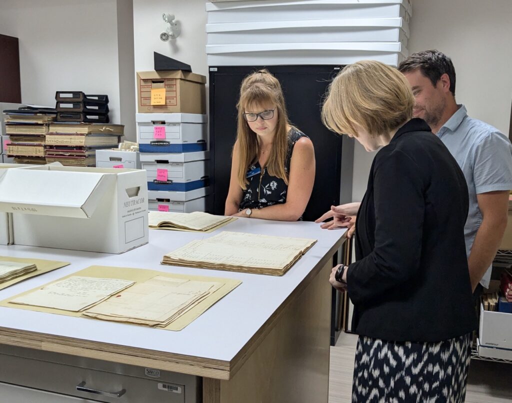 Staff members of the Peterborough Museum and Archives with Janice McGann gather around a table displaying documents from the emigration.