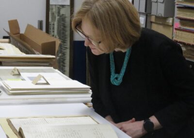 Consul General Janice McGann leaning over to inspect an old hand written journal from the Peter Robinson Emigration. In the background other documents are on display.