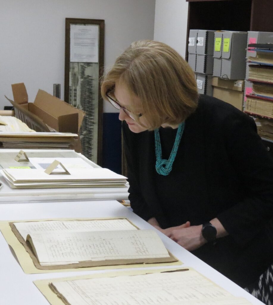 Consul General Janice McGann leaning over to inspect an old hand written journal from the Peter Robinson Emigration. In the background other documents are on display.