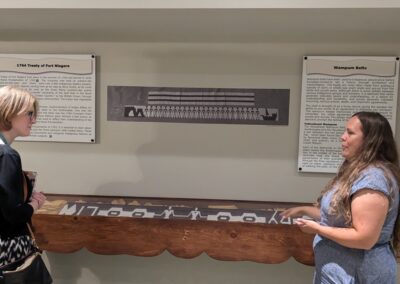 Ruth O'Connell on the right of the Aabnaabin Exhibit explaining, while Consul General Janice McGann and Daniel Capistrano on the right observe their explanation.