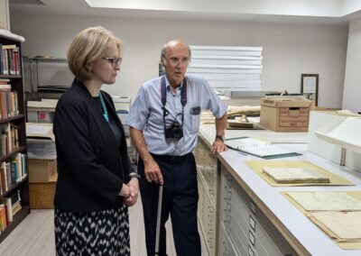 Janice McGann stands next to Dennis Carter-Edwards while they look over displayed emigration documents presented on an archive desk.